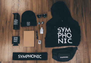 A collection of branded items labeled "SYMPHONIC," including a hoodie, beanie, water bottle, and more, displayed on a wood floor—perfect for fans heading to Amsterdam Dance Event.